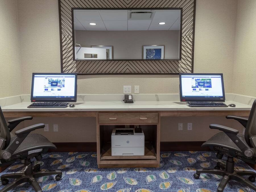 Habitación de hotel con un escritorio que tiene dos computadoras portátiles, una impresora y dos sillas de oficina.