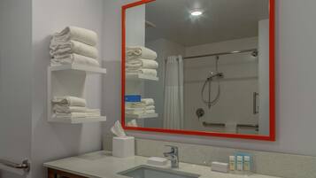 A bathroom with a large mirror, a sink, and shelves with folded towels.