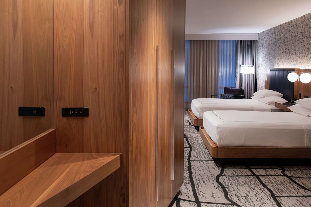 A hotel room with two beds, a wooden wardrobe, a desk, and a patterned carpet.