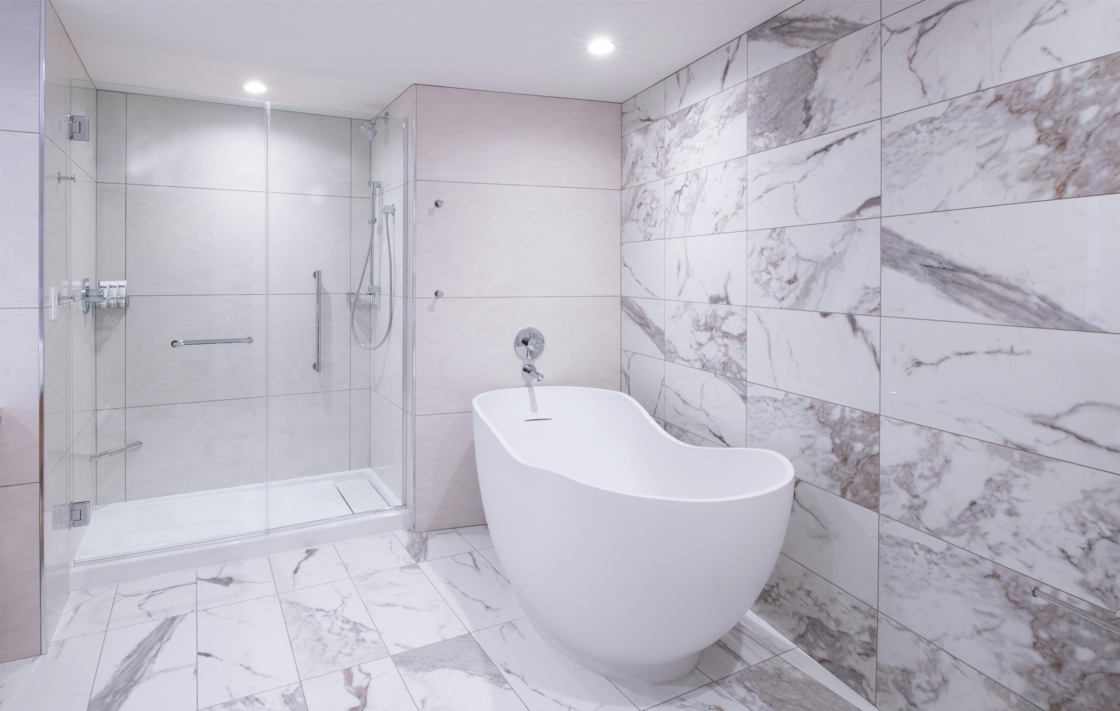 A modern bathroom with a glass-enclosed shower, a freestanding bathtub, and marble-tiled walls.