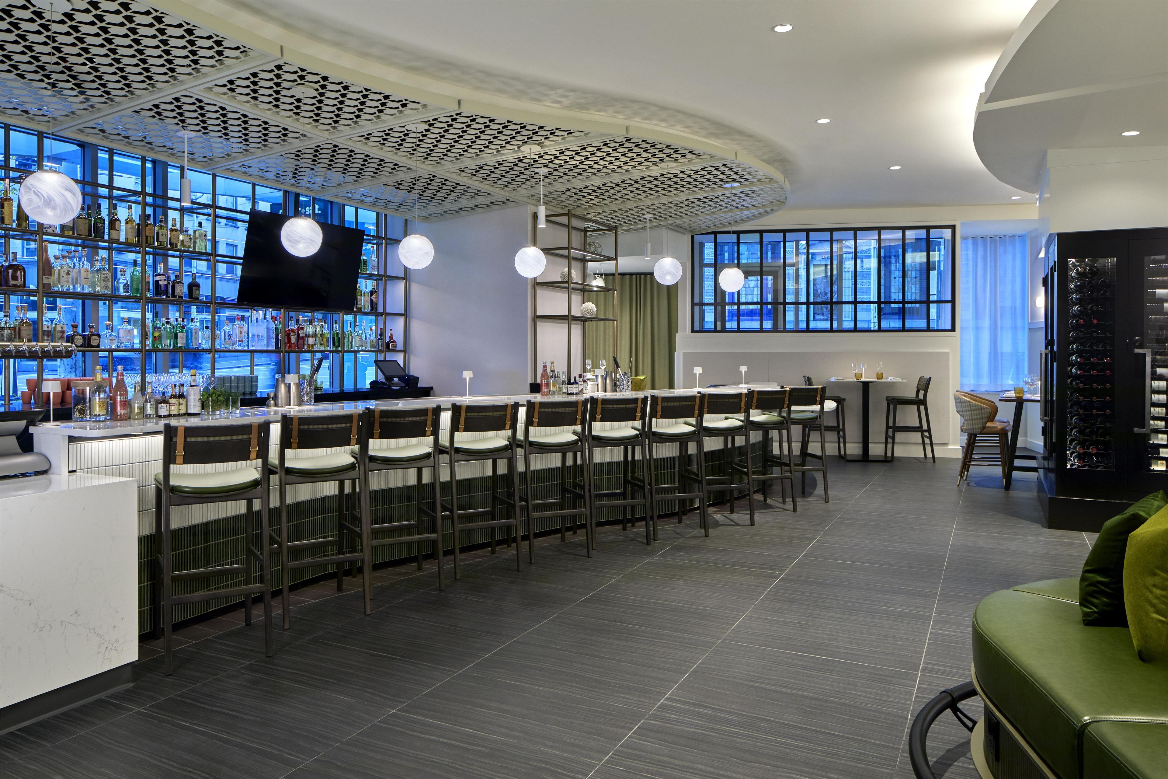 A bar area with a long counter, multiple bar stools, and a television screen.