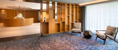 A modern hotel lobby with a reception desk, seating area, and a large window with curtains.