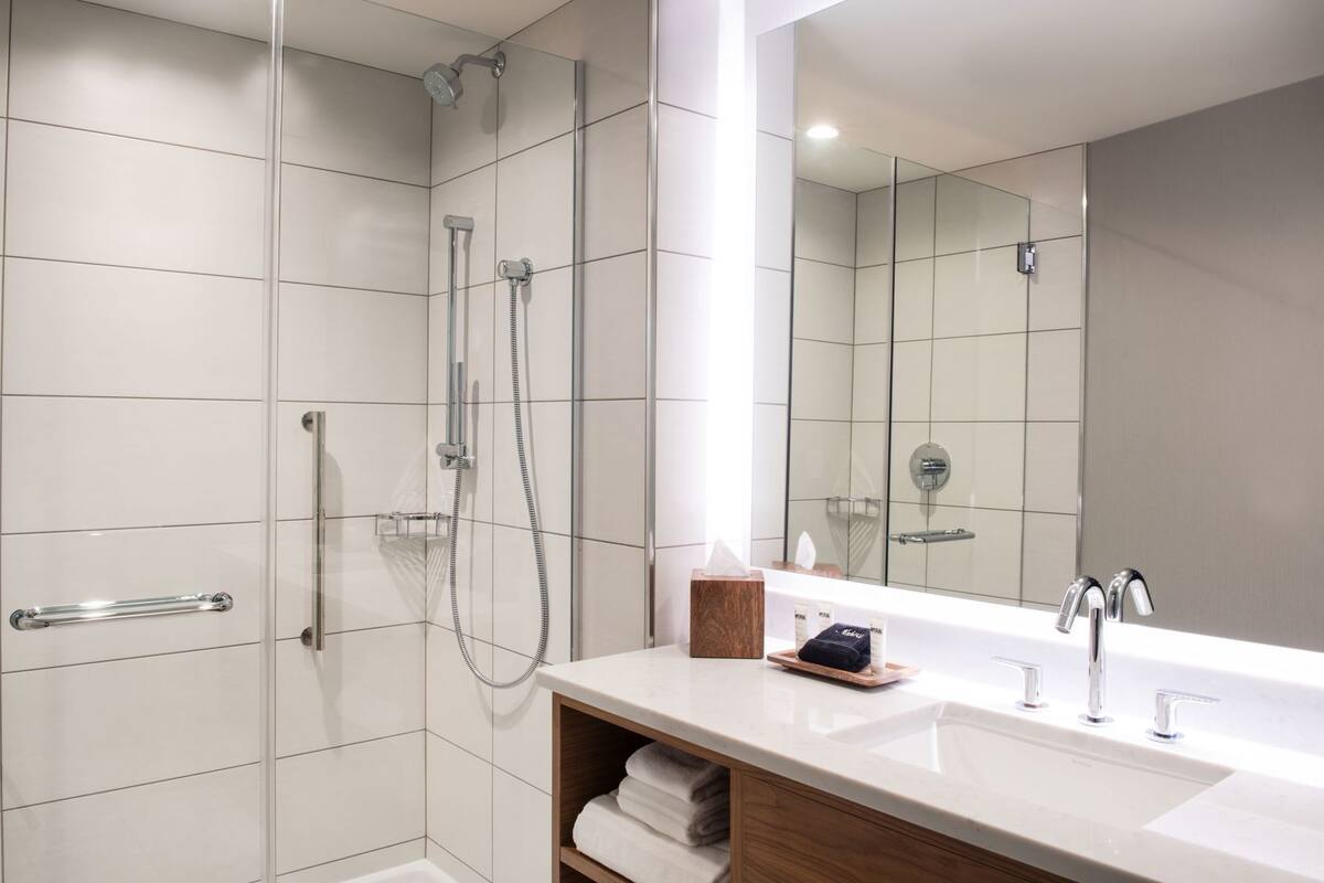 Un baño moderno con cabina de ducha de vidrio, un espejo grande y un mueble de tocador con lavamanos y espacio para toallas.