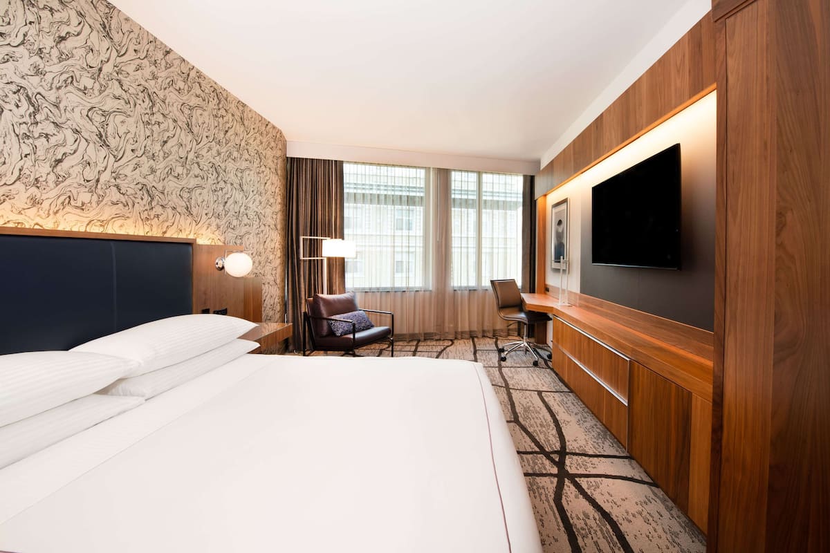 A hotel room with a large bed, a desk, a chair, a TV, and a window with curtains.