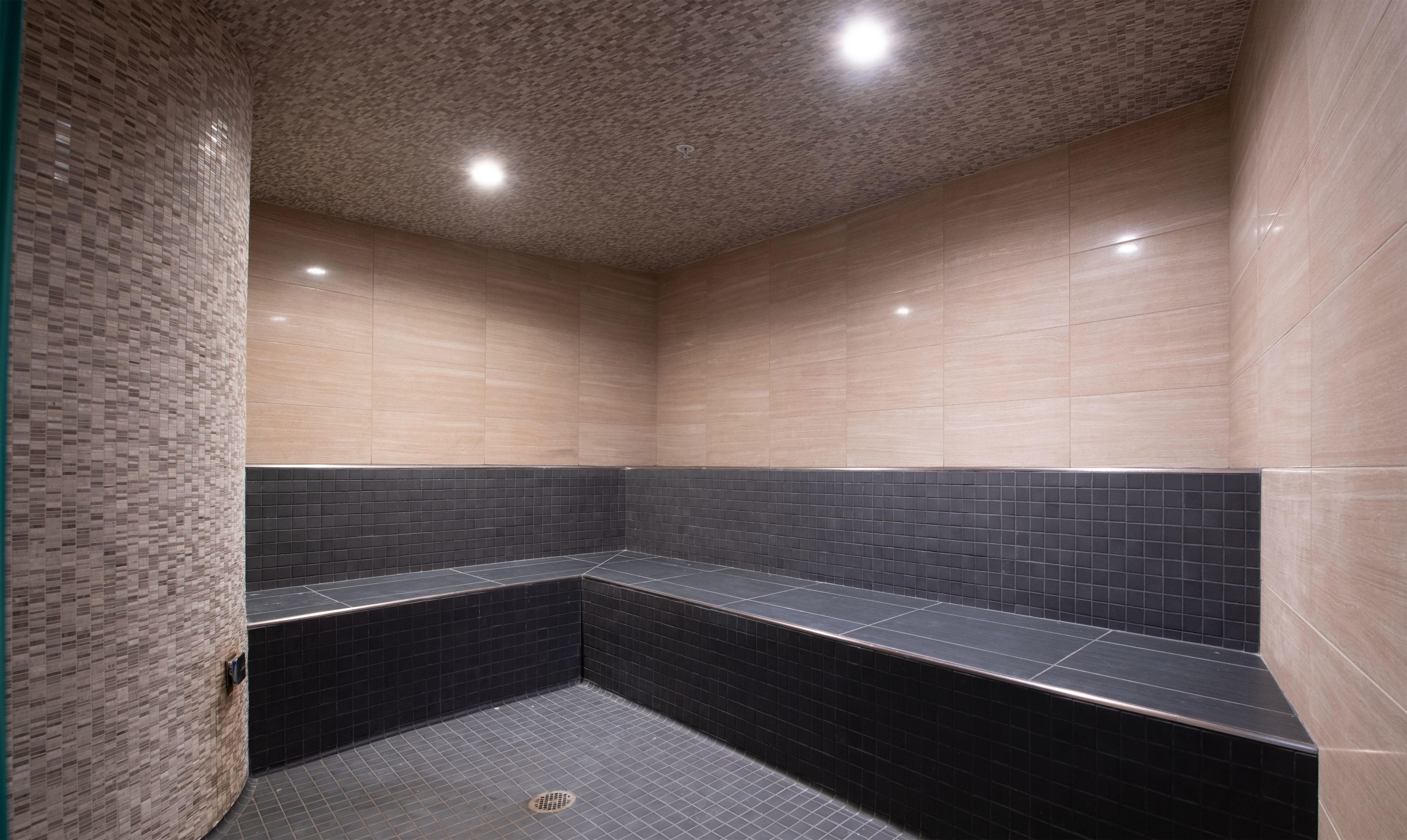 A modern bathroom with a tiled floor, a bench, and a ceiling with recessed lighting.