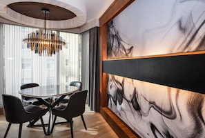 Un comedor moderno con una mesa redonda de vidrio, sillas negras, una lámpara colgante original y un cuadro abstracto grande en la pared.