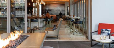 A modern bar area with seating, a fire feature, and a view of the cityscape.