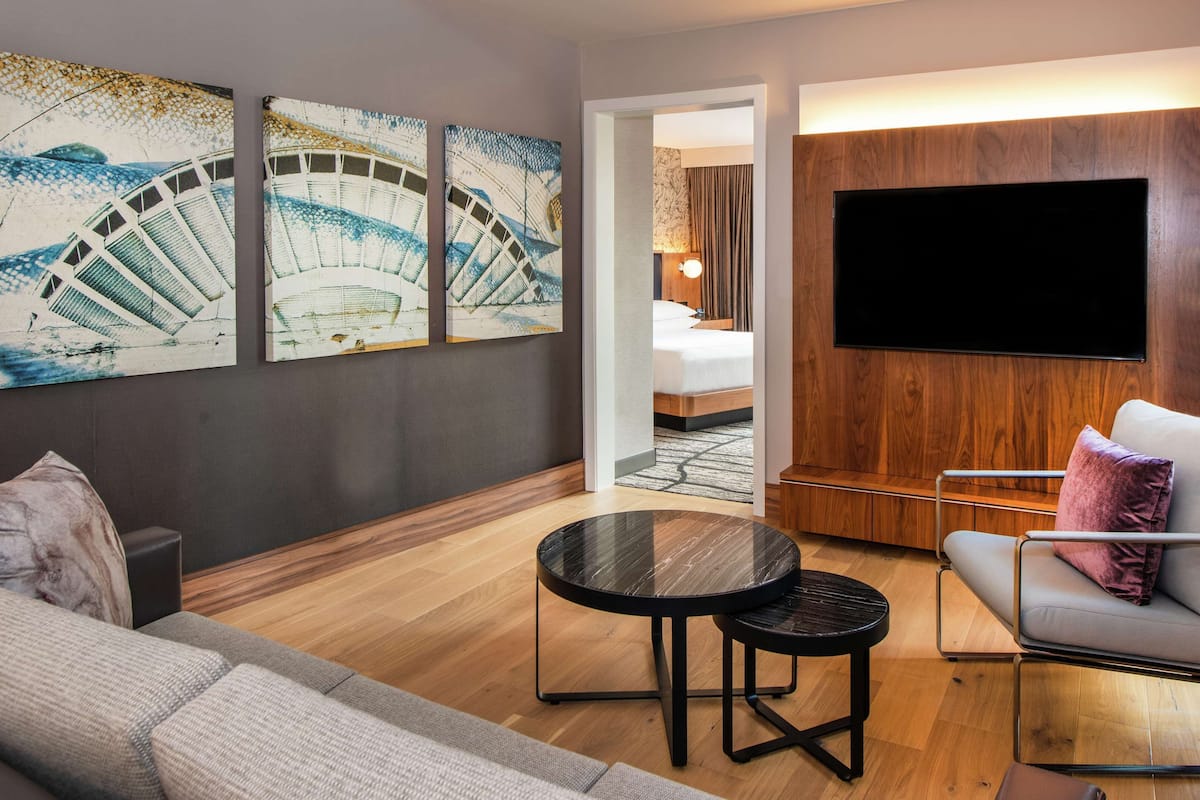 A modern hotel room with a sofa, a chair, a small table, and three artworks on the wall.