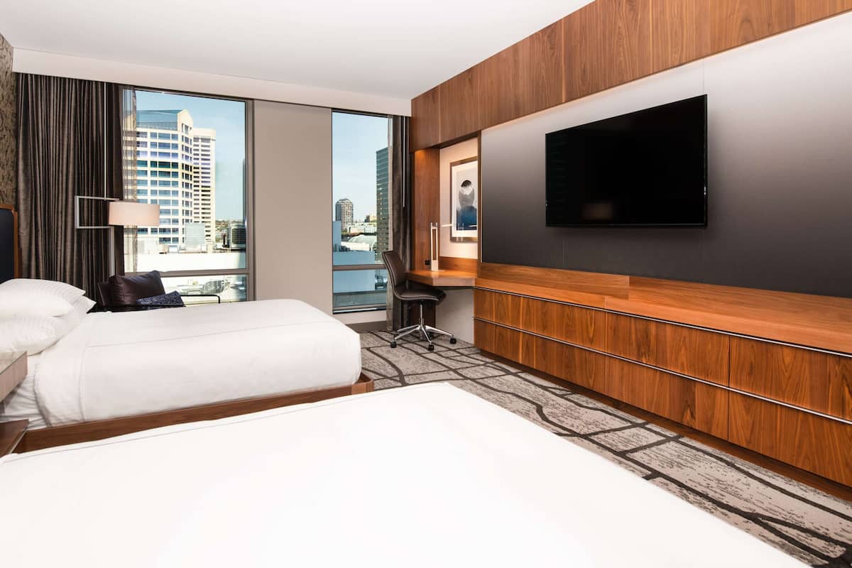 A hotel room with a large bed, a desk, a chair, a flat-screen TV, and a view of the city.
