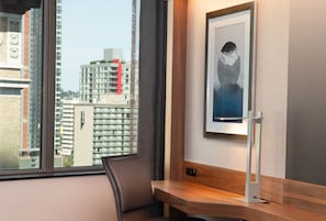 Une chambre d’hôtel avec une grande fenêtre, un bureau, une chaise et un tableau encadré au mur.