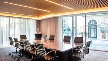A conference room with a large table and modern chairs, large windows with curtains, and a city view.