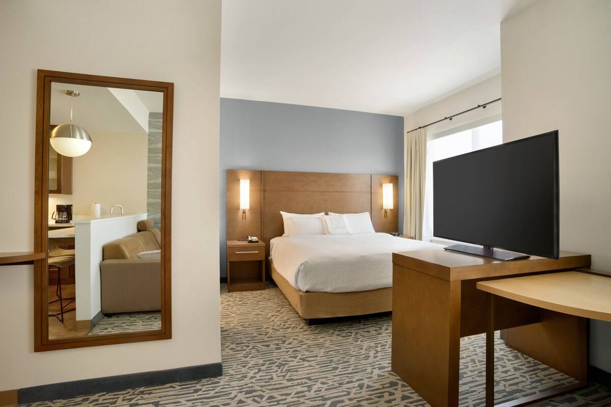 A hotel room with a bed, bedside table, TV, and a mirror.