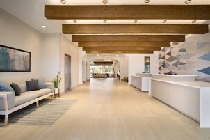 Un moderno área de recepción con techo de madera, una mesa de recepción y un espacio de espera con sofá y planta.