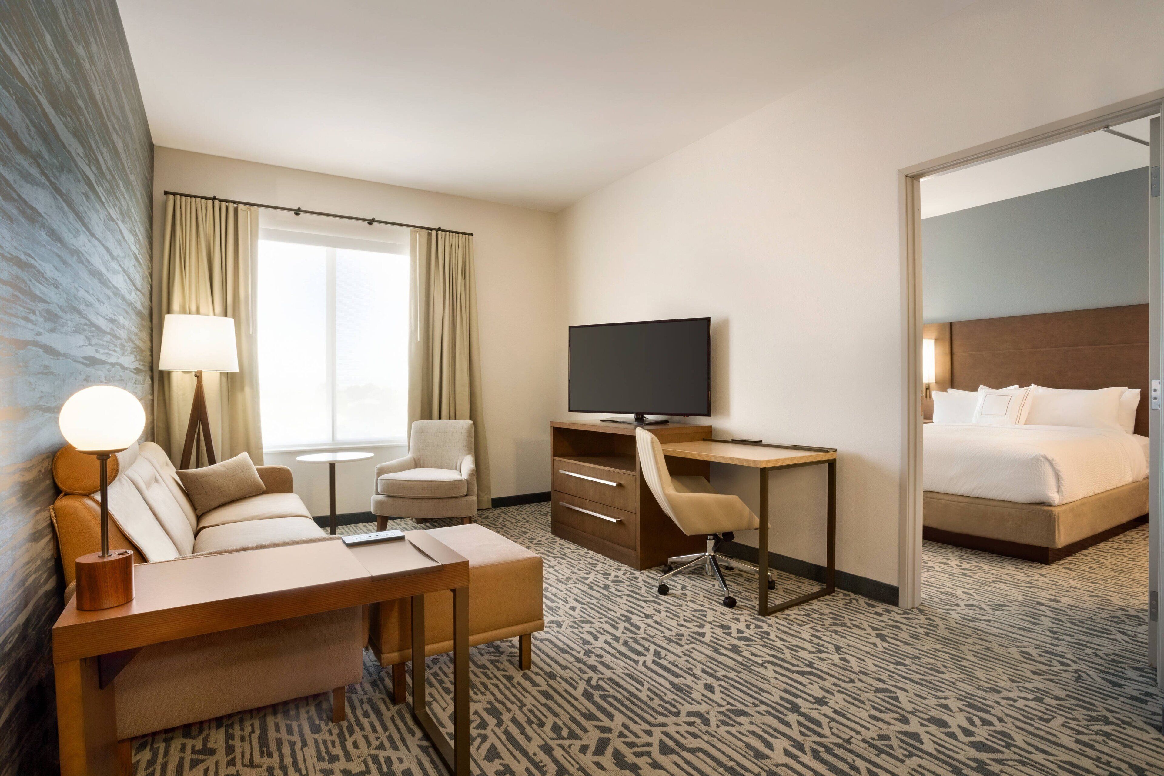 Ein Hotelzimmer mit einer Couch, einem Schreibtisch, einem Fernseher und einem Bett.