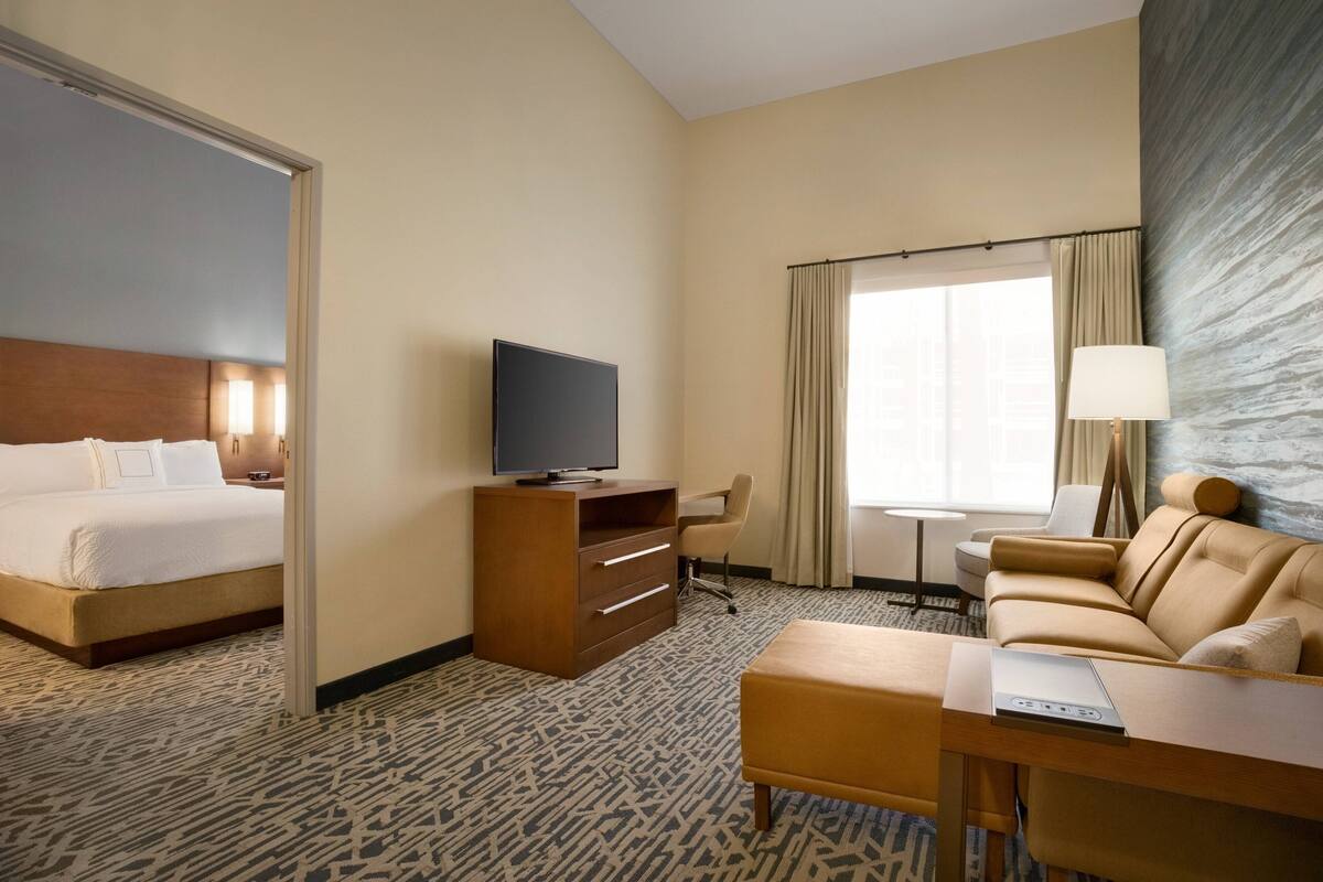A hotel room with a bed, a desk, a television, a sofa, and a window with curtains.