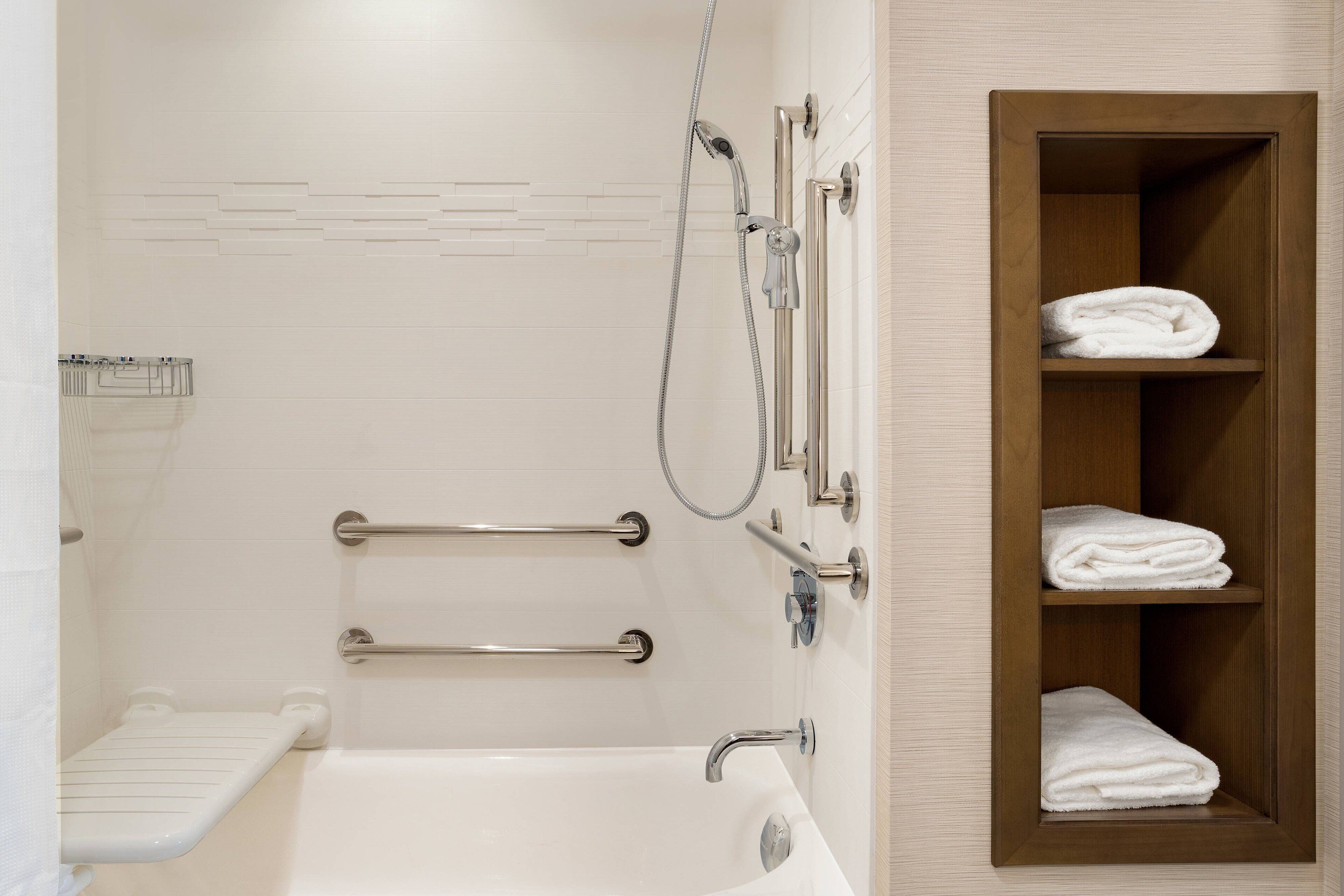 Une salle de bain avec une baignoire, une douche et une étagère en bois où sont posées des serviettes.