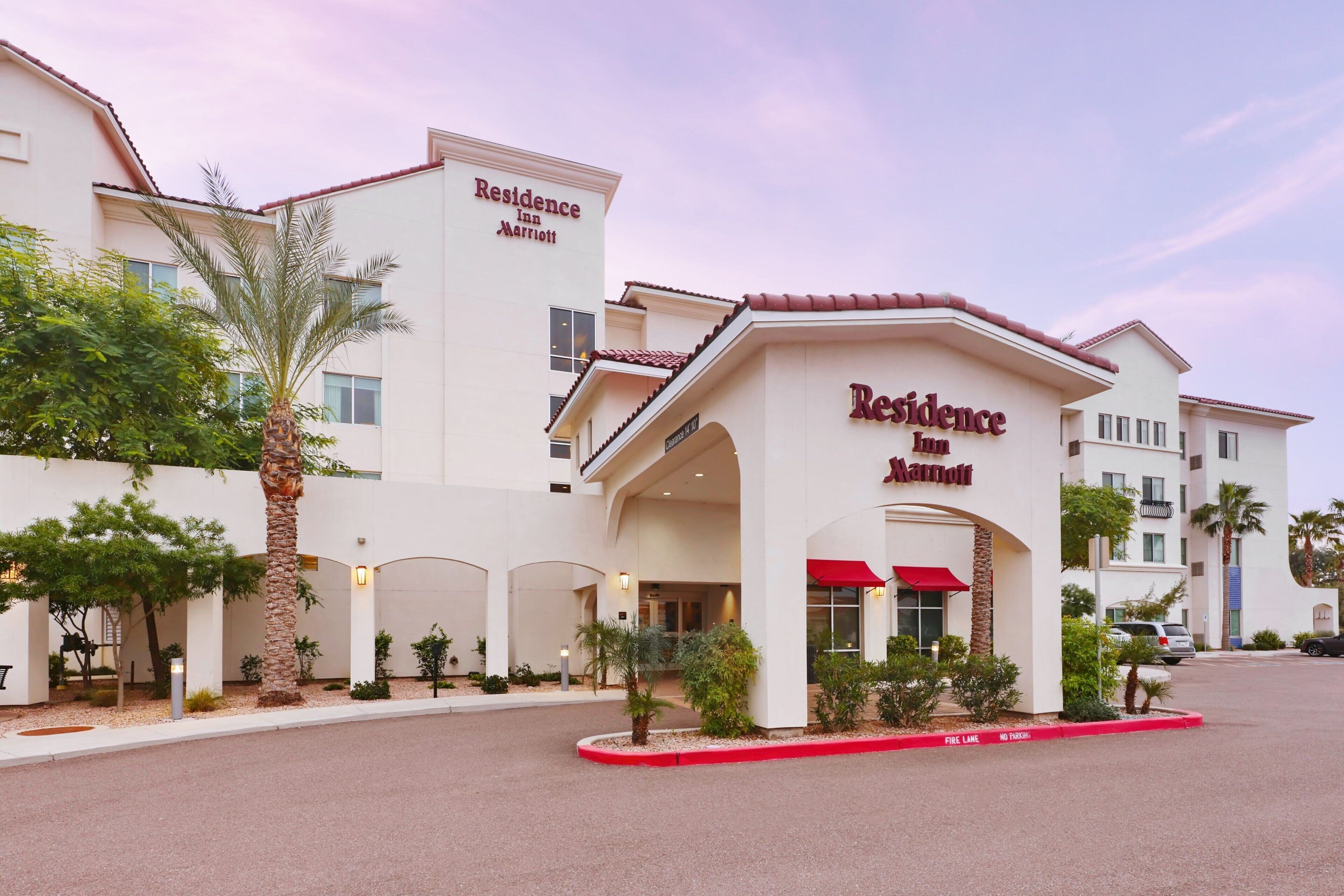 A hotel entrance with a red awning, palm trees, and a clear sky.
