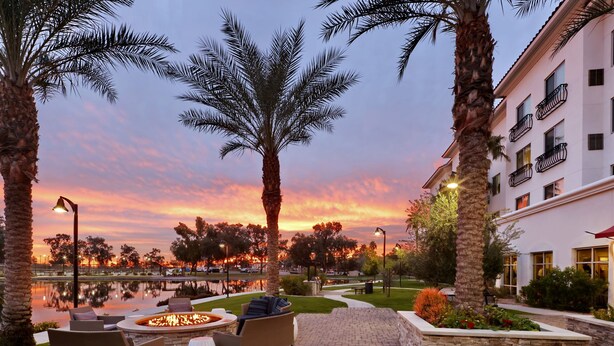 A patio area with outdoor seating and a fire pit, surrounded by palm trees and a building with balconies. - Residence Inn by Marriott Phoenix Chandler/South (Chandler)