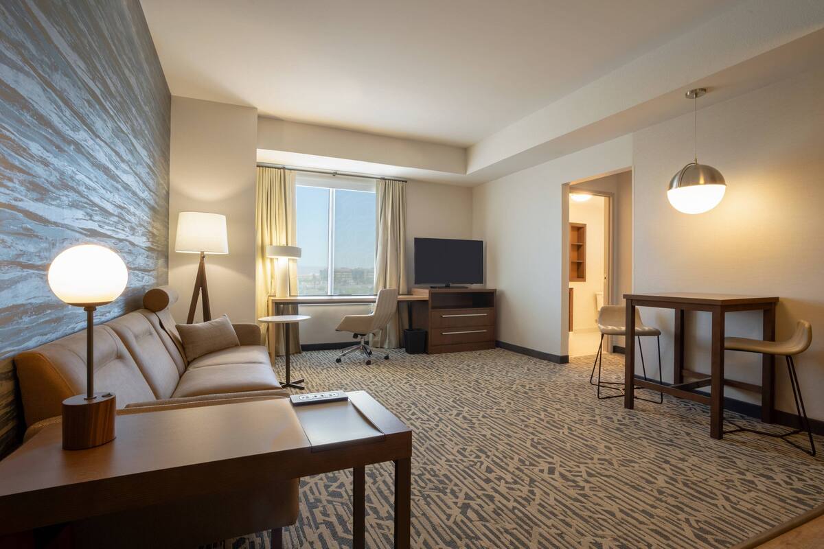 A hotel room with a sofa, a desk, a TV, and a dining table.