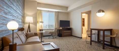 Hotellihuone, jossa on sohva, työpöytä, televisio ja ruokapöytä.