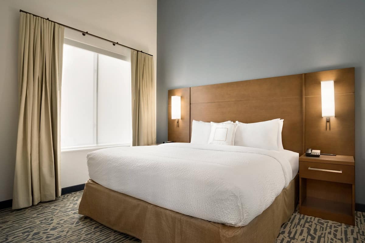 A hotel room with a large bed, a nightstand, a lamp, and a window with curtains.