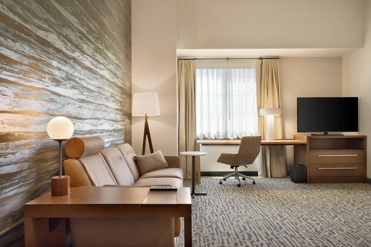 A hotel room with a sofa, a desk, a television, and a lamp.
