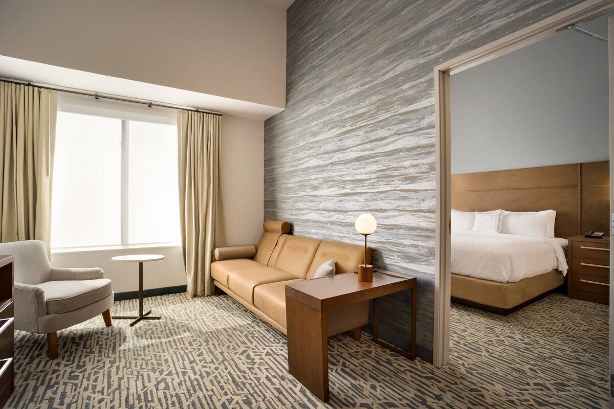 A hotel room with a sofa, a small table with a lamp, a bed, and a large mirror.