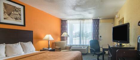 A hotel room with a bed, a desk with a computer, a TV, and a window with curtains.