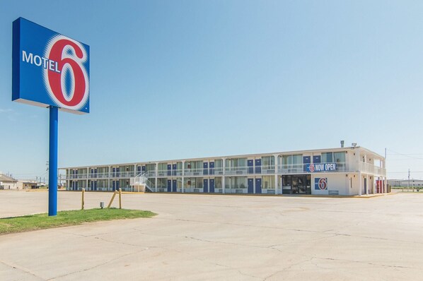 A motel with a large sign reading "Motel 6" and a "NOW OPEN" sign on the building.