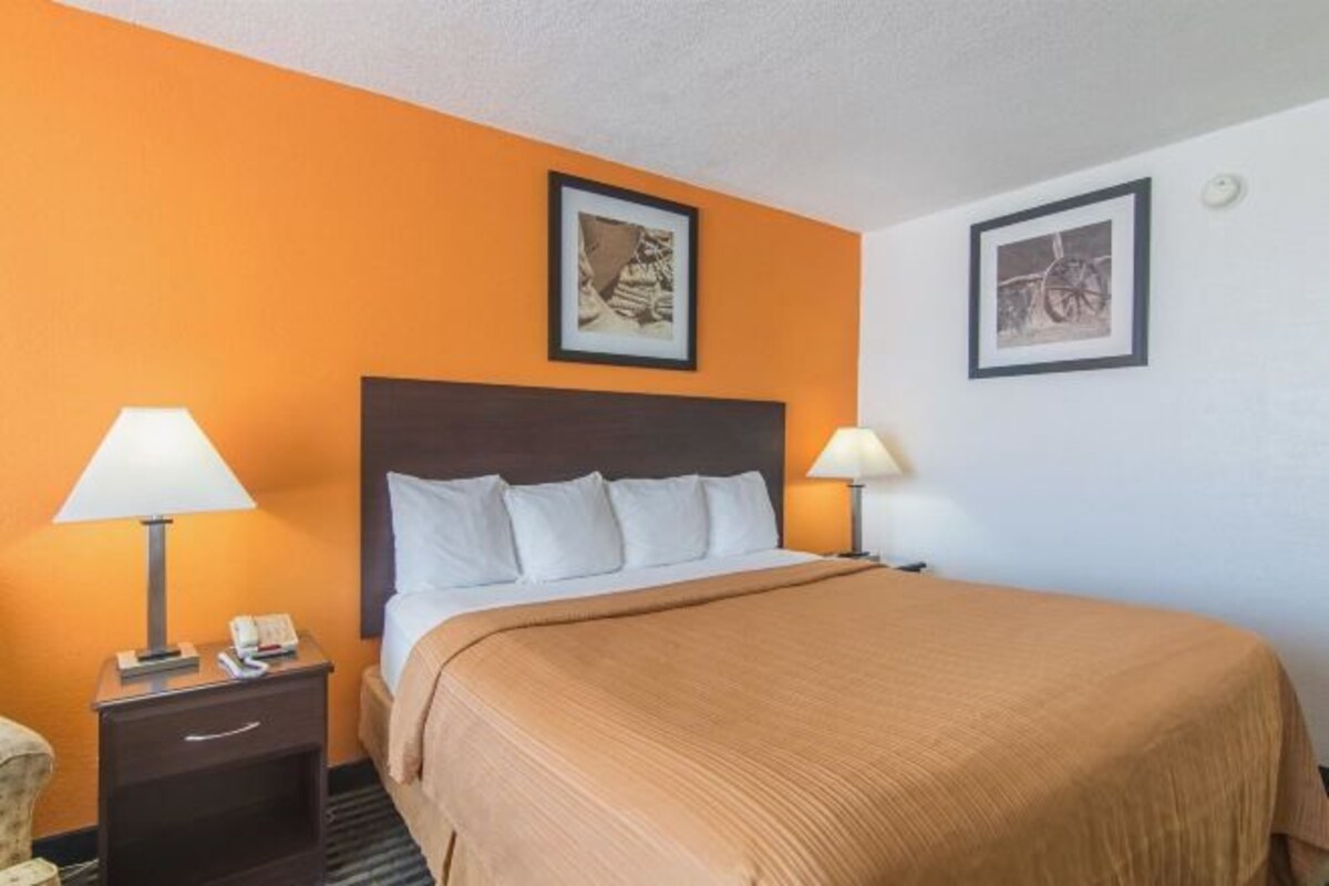 A hotel room with a large bed, two bedside lamps, a nightstand with a phone, and two framed pictures on the walls.