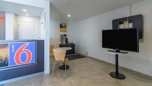 Moderni hotellihuone, jossa on suuri televisio, kahvinkeitin ja pieni oleskelualue.