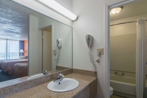 Un baño de hotel con lavamanos, espejo, secador de pelo y ducha.