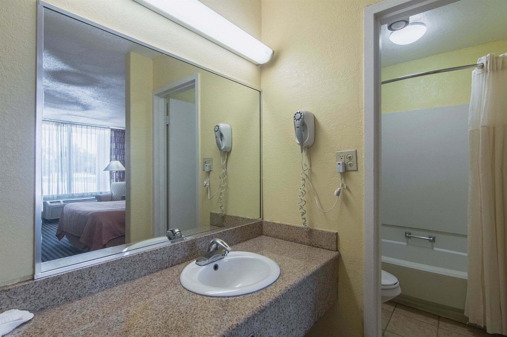 A bathroom with a granite countertop, a white sink, a mirror, and two hair dryers mounted on the wall.