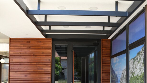 Une entrée moderne, avec une façade en bois, une porte en verre et une vue sur un paysage montagneux grâce à de grandes fenêtres.