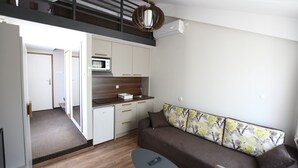 Un appartement moderne doté d’une kitchenette, d’un canapé agrémenté de coussins à motifs floraux et d’un escalier menant à un niveau supérieur.