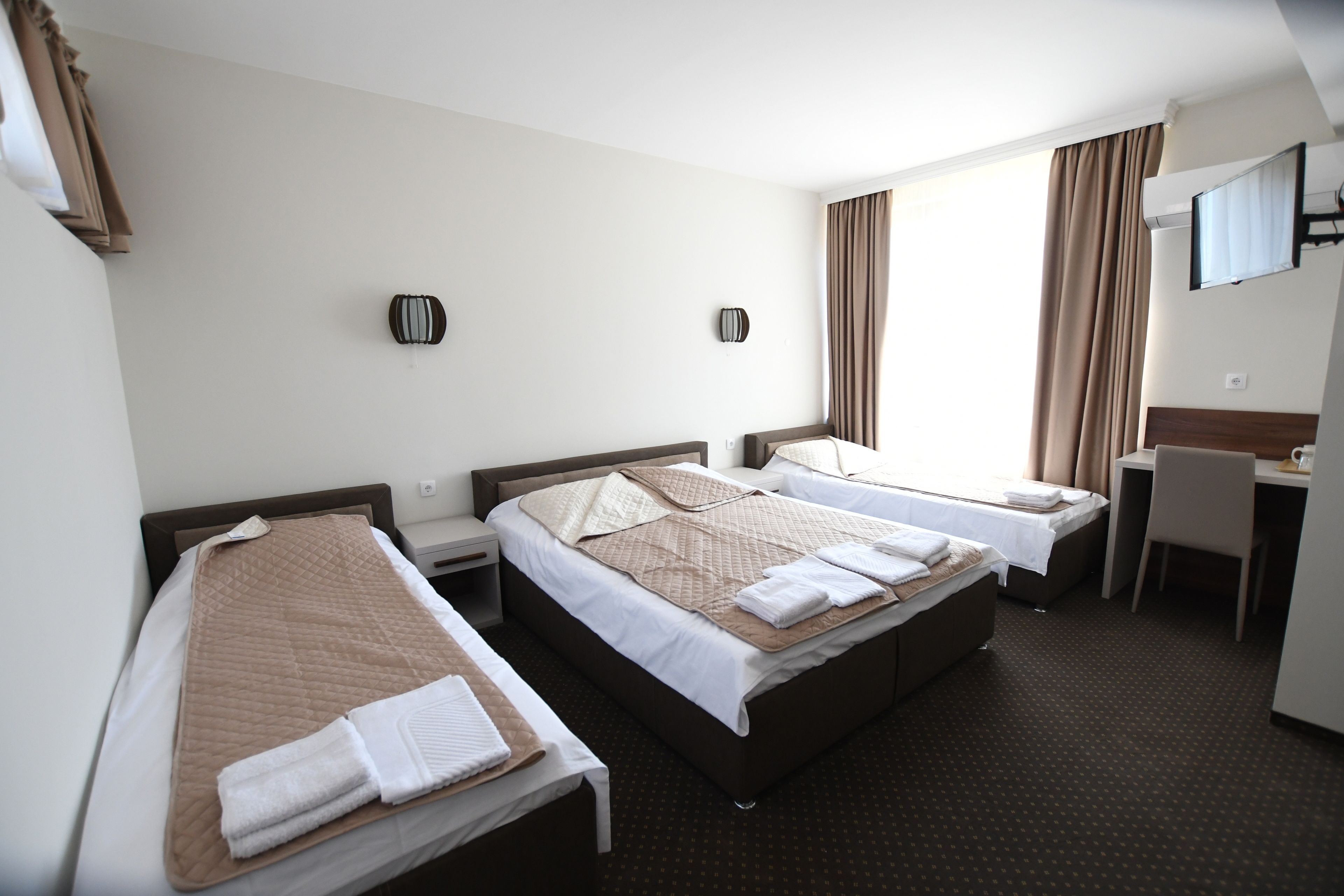 A hotel room with two single beds, a desk, and a TV.