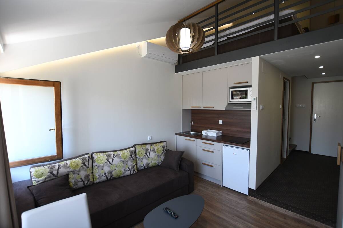 Um apartamento moderno com sala de estar, cozinha compacta e escada que leva a um andar superior.