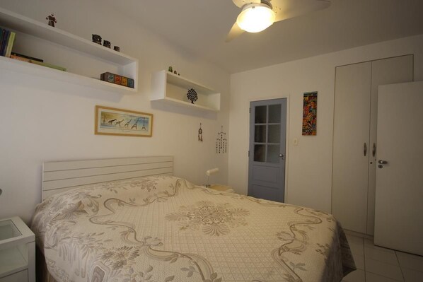 A bedroom with a bed, a wardrobe, a door, and shelves with items.