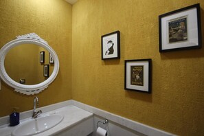 A bathroom with a white sink, a round mirror with a scalloped edge, and two framed pictures on the wall.