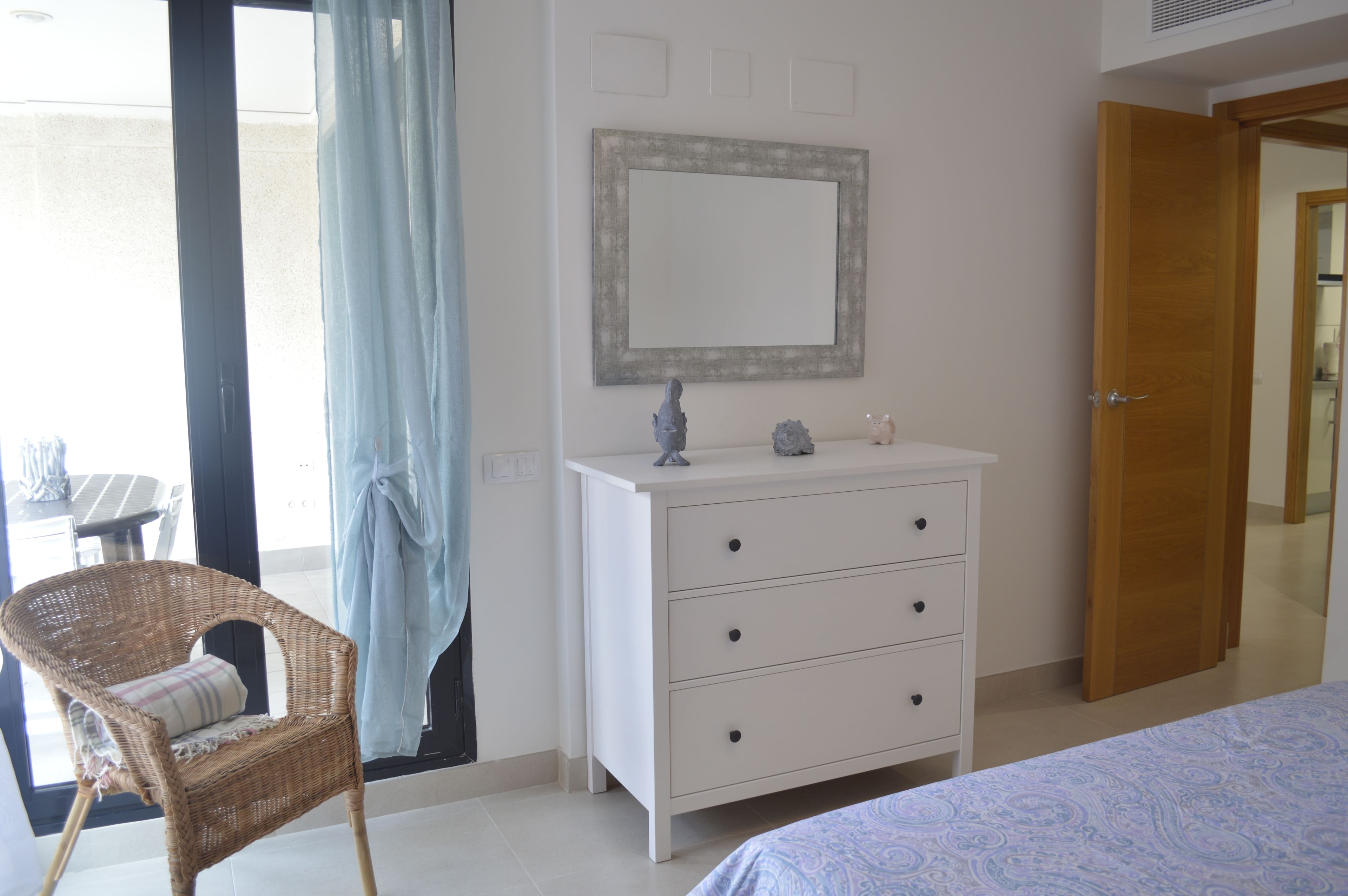 Un dormitorio con cama, cómoda, silla, espejo y puerta.