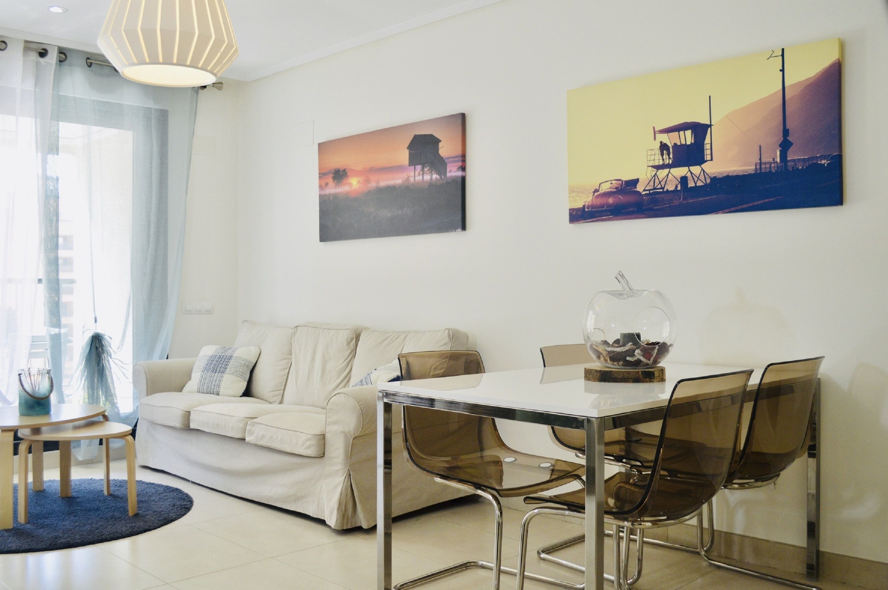 Een moderne woonkamer met een bank, een glazen eettafel en stoelen. Twee schilderijen hangen aan de muur.