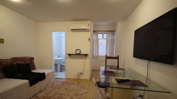 A living room with a sofa, a glass table, a TV, and a kitchen area in the background. - GoHouse Djalma 519 (Rio de Janeiro)