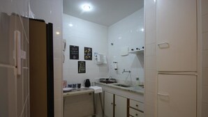 A compact kitchen with white tiles, a sink, a coffee maker, and a refrigerator. - GoHouse Djalma 519 (Rio de Janeiro)