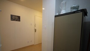 A hallway with a door, a trash bin, and a refrigerator with a water dispenser on top. - GoHouse Djalma 519 (Rio de Janeiro)