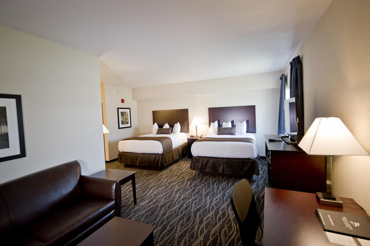 A hotel room with two beds, a desk, a chair, a sofa, and a lamp.
