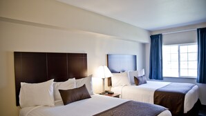 A hotel room with two beds, a nightstand with a lamp, and a window with curtains. - Cobblestone Inn & Suites - Clarinda (Clarinda)