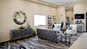 A hotel lobby with a grey sofa, patterned carpet, a decorative wall piece, and a television on the wall. - Cobblestone Inn & Suites - Clarinda (Clarinda)