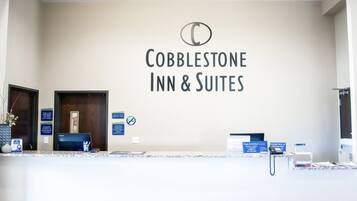 A reception desk at Cobblestone Inn & Suites with a sign above it, a computer, and a telephone.