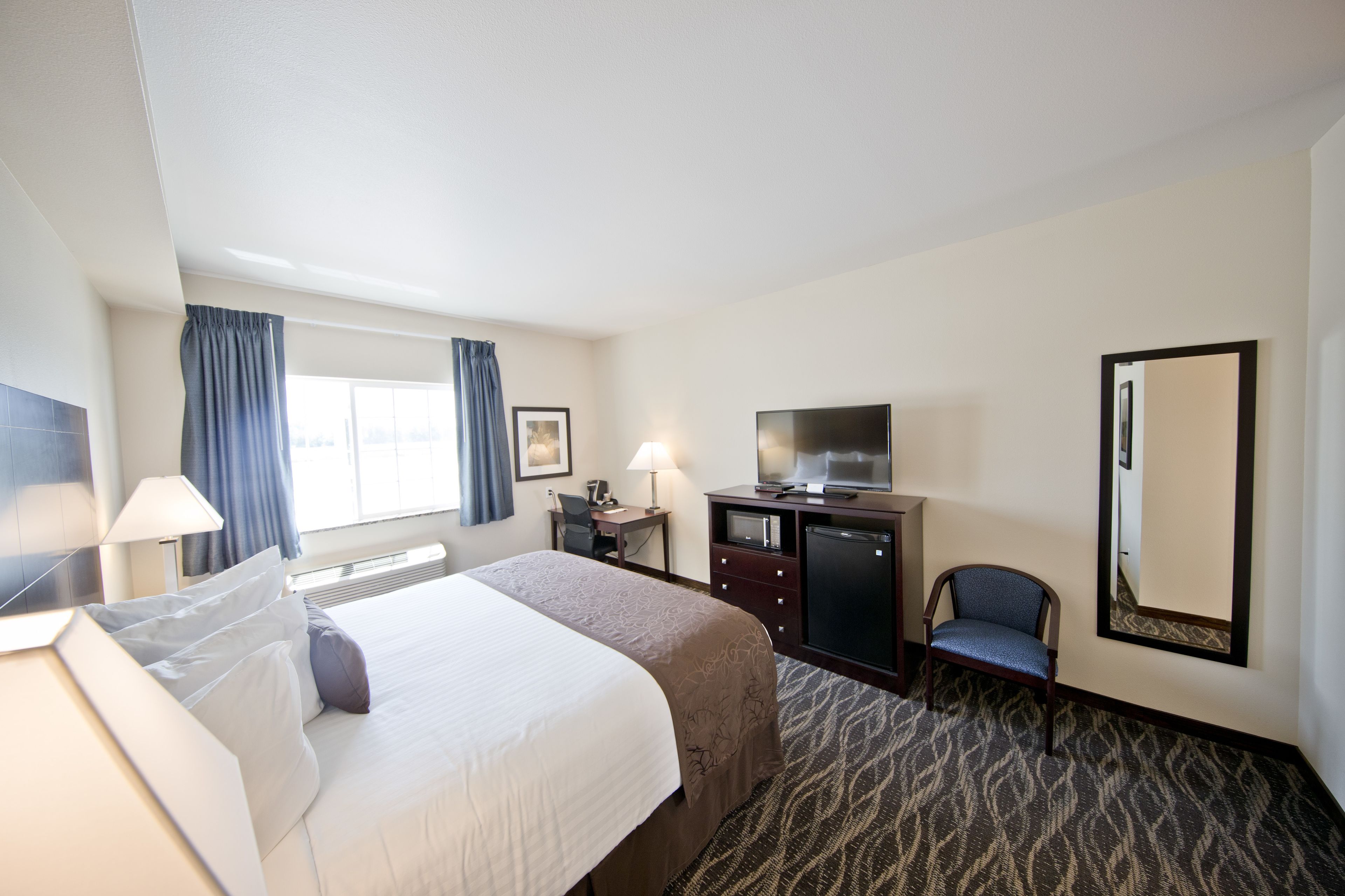 A hotel room with a bed, desk, chair, TV, and a large mirror.