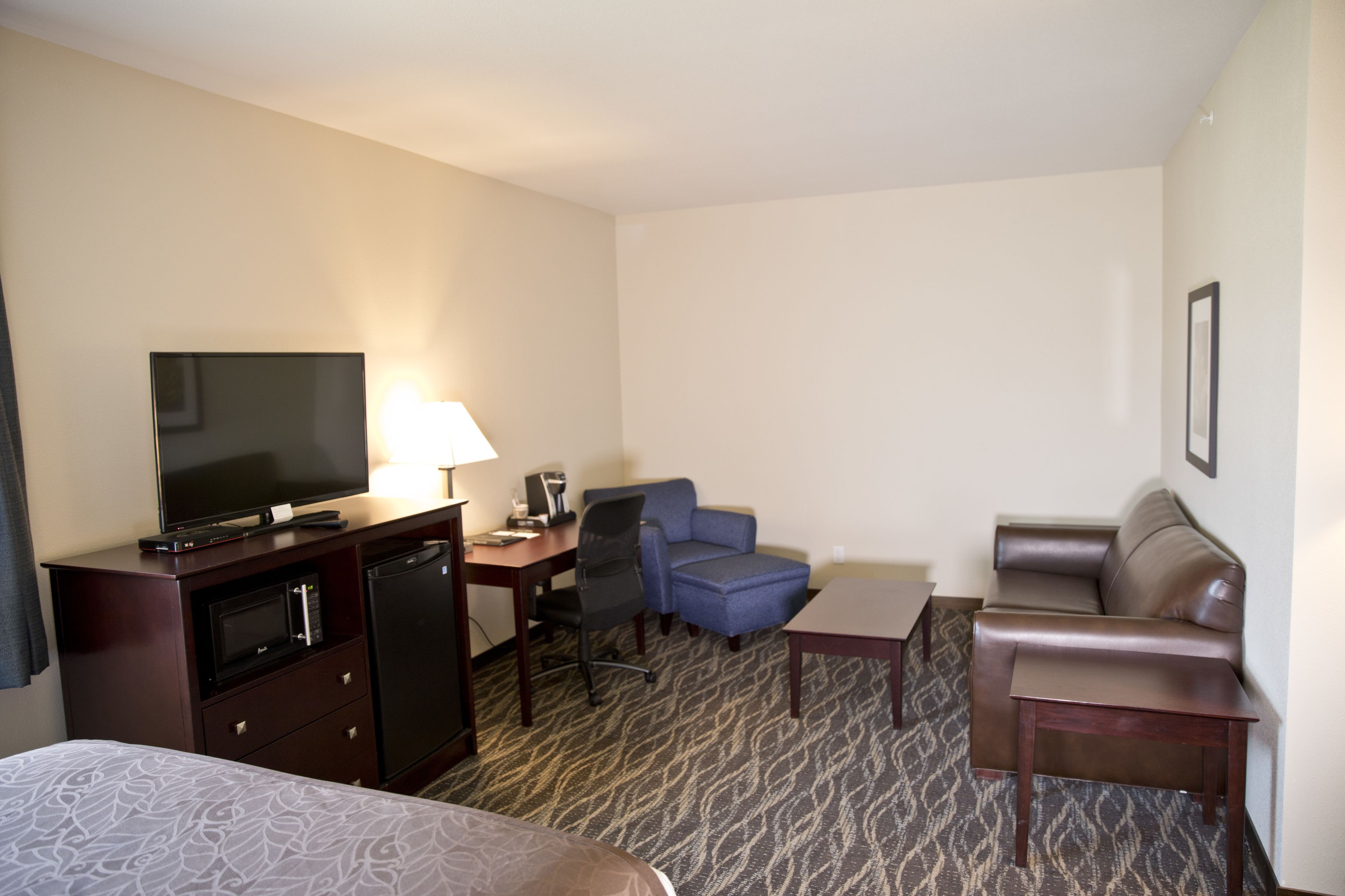 A hotel room with a bed, a desk with a computer, a television, a chair, a sofa, and a small table.
